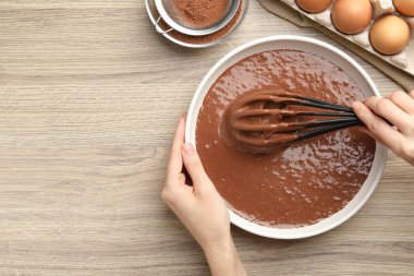 Kadın, ahşap masada çikolatalı hamuru çırpıyla karıştırıyor. Metin için boşluk