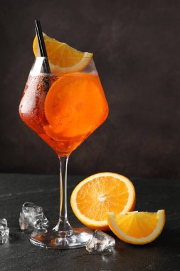 Bir bardak ferahlatıcı spritzer kokteyli, buz küpleri ve siyah masada portakal dilimleri.