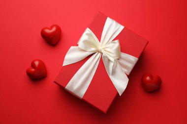 Güzel bir hediye ve kırmızı arka planda dekoratif kalpler, düz yatış. Sevgililer Günü