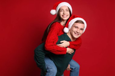 Noel Baba şapkalı gülümseyen çift kırmızı arka planda eğleniyor. Mutlu Noeller ve mutlu yıllar.