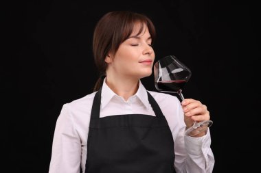 Profesyonel şarap garsonu siyah arka planda kırmızı şarap tadıyor.