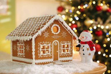Güzel zencefilli kurabiye evi, kardan adam figürü ve kapalı alanda bulanık ışıklara karşı suni kar, yakın plan. Noel atmosferi