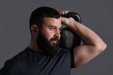 Gri arka planda kettlebell ile egzersiz yapan adam.