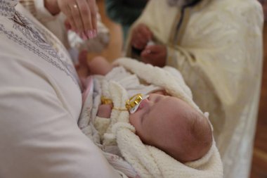 Anne, vaftiz töreninde çocuğunu kucağında tutuyor.