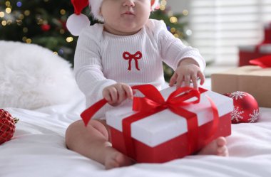 Noel Baba şapkalı şirin bir bebek. Evde yatağında hediyeler ve takılar var. Noel sezonu