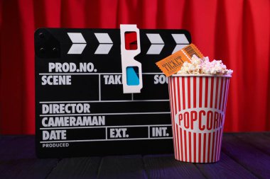 Kağıt bardakta lezzetli patlamış mısır, sinema bileti ve kırmızı perdelere karşı mor ahşap masa üzerindeki yazı tahtası.