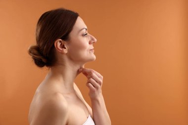 Güzel bir kadın soluk turuncu arka planda boynuna dokunuyor.