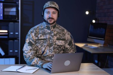 Askerlik. Kulaklıklı bir asker, gece ofiste ahşap masada çalışıyor.