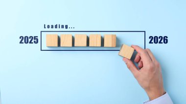 Yeni yıl 2026. Bir adam açık mavi arka planda yükleme çubuğuna diğerlerinin yanına ahşap küp koyar, üst görünüm