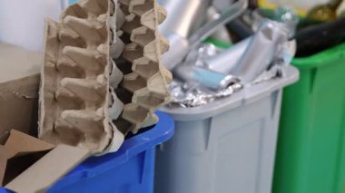 Açık mavi arka planda çöp kutuları var, kamera sağa hareket ediyor. Atık sıralama