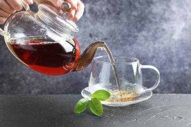 Siyah masada çaydanlıktan fincana sıcak çay dolduran kadın, yakın plan.