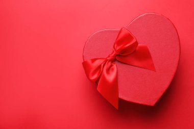 Sevgililer Günün kutlu olsun. Kırmızı arka planda kalp şeklinde hediye kutusu, üst manzara. Metin için boşluk