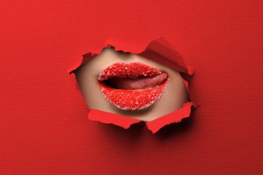 Şekerli dudakları olan güzel bir kadın, kırmızı kağıttaki yırtık delikten bakıyor.