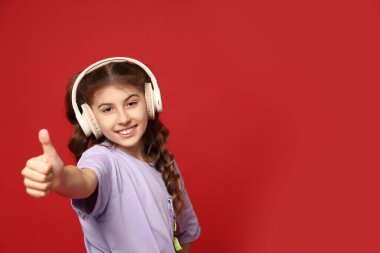 Kulaklıklı gülümseyen kız kırmızı arka planda baş parmağını gösteriyor. Metin için boşluk