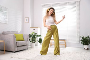 Kulaklıklı mutlu kadın evde dans ediyor.