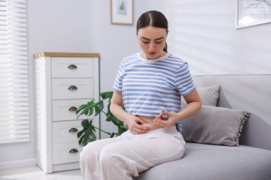 In vitro fertilisation. Woman making injection into her belly on sofa indoors