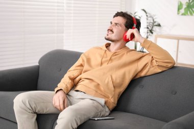 Kulaklıklı mutlu adam evdeki kanepede müzik dinliyor.