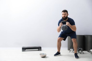 Güçlü adam spor salonunda kettlebell ile egzersiz yapıyor, mesaj için yer var.