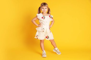 Sarı arka planda poz veren sevimli küçük kız.