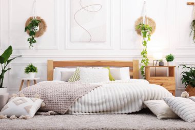 Rahat yatağı, yastıkları, lambası ve farklı çiçekleri olan güzel bir oda.