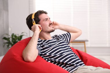 Kulaklıklı gülen adam evdeki koltukta müzik dinliyor.