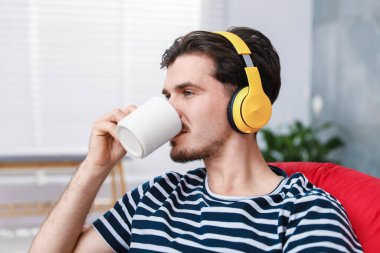 Kulaklıklı genç adam evde müzik dinliyor.