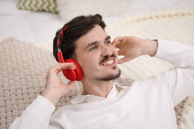 Kulaklıklı gülümseyen adam yatakta müzik dinliyor.