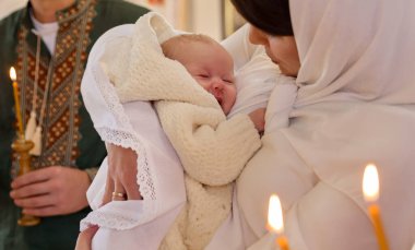 Anne, vaftiz töreninde çocuğunu kucağında tutuyor.