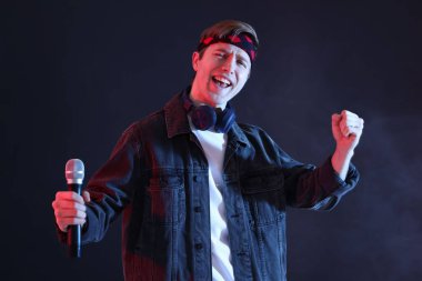 Kulaklıklı ve mikrofonlu bir adam karanlık arka planda dumanlı.