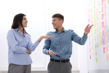 Meslektaşlar, ofiste yapışkan notlarla beyaz tahtaya yakın stratejileri tartışıyor