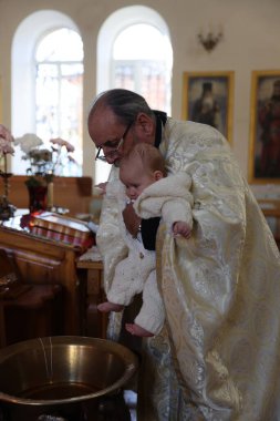 Mykolaiv, Ukrayna - 1 Kasım 2025: Papaz vaftiz töreni sırasında çocuğu vaftiz fontuna koydu