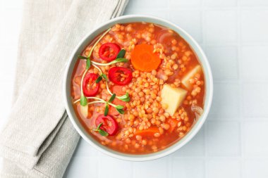 Lezzetli mercimek çorbası. Kasede sebzeler, beyaz fayanslı masa, üst manzara.