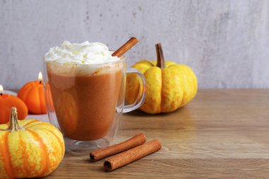 Cam bardakta kremalı balkabaklı latte, tarçın çubukları, taze sebzeler ve ahşap masada yanan mumlar, yakın plan. Metin için boşluk