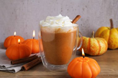 Cam bardakta kremalı balkabaklı latte, tarçın çubukları, taze sebzeler ve ahşap masada yanan mumlar, yakın plan.