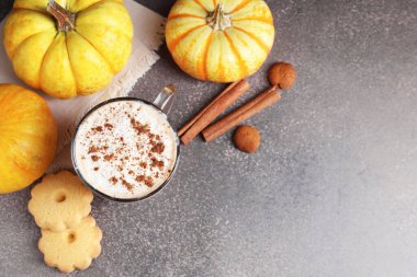 Fincanda balkabaklı latte, baharatlar, kurabiyeler ve gri desenli masada taze sebzeler. Metin için boşluk