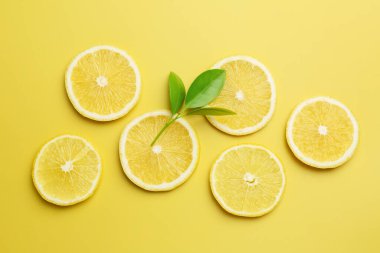 Taze limon dilimleri ve sarı arka planda yapraklar, düz uzanmış.