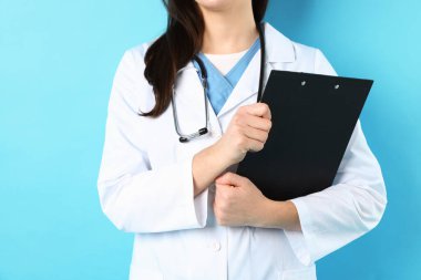 Açık mavi arka planda panosu ve steteskopu olan doktor, yakın plan.