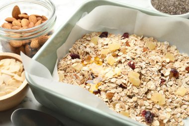 Tahıl yapıyorum. Yulaf gevreği, kurutulmuş meyve, badem fıstığı ve bal beyaz masada, yakın plan.