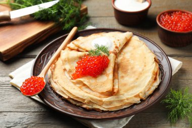 Kırmızı havyarlı lezzetli krepler, ekşi krema ve ahşap masada dereotu, yakın plan.