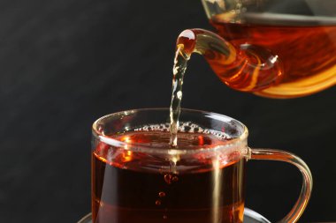 Siyah arka planda çaydanlıktan fincana sıcak çay dökmek, yakın plan. Metin için boşluk