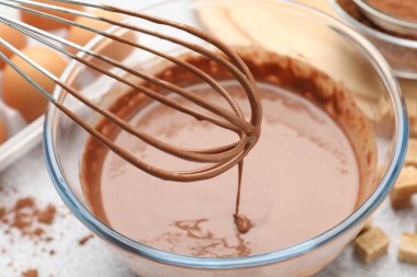 Gri masada çikolata hamuru kabın içine damlıyor, yakın plan.