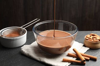 Sıvı çikolata hamuru siyah masada cam kaseye akıyor, yakın plan.