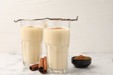 Bardaklarda lezzetli protein karışımı, tarçın ve beyaz mermer masada vanilya kapsülleri, yakın plan.