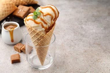 Tuzlu karamel soslu lezzetli dondurma ve gri masada naneli waffle konisi, yakın plan. Metin için boşluk