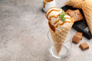 Tuzlu karamel soslu lezzetli dondurma ve gri masada naneli waffle konisi, yakın plan. Metin için boşluk