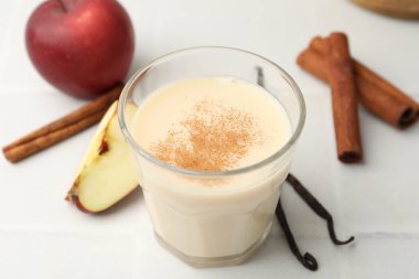 Bardakta lezzetli protein karışımı, tarçın, elma ve vanilya kapsülleri beyaz masada, yakın plan.