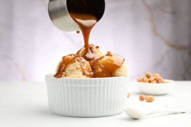 Lezzetli dondurmanın üzerine karamel sosu dökmek. Beyaz masada badem, yakın plan.