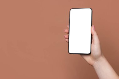 Kahverengi arka planda boş ekranlı akıllı telefonu olan bir kadın, yakın plan. Tasarım için model