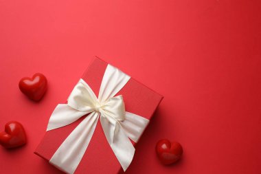 Güzel bir hediye ve kırmızı arka planda dekoratif kalpler, metin için yeri olan düz bir yer. Sevgililer Günü