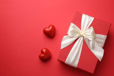 Güzel bir hediye ve kırmızı arka planda dekoratif kalpler, metin için yeri olan düz bir yer. Sevgililer Günü